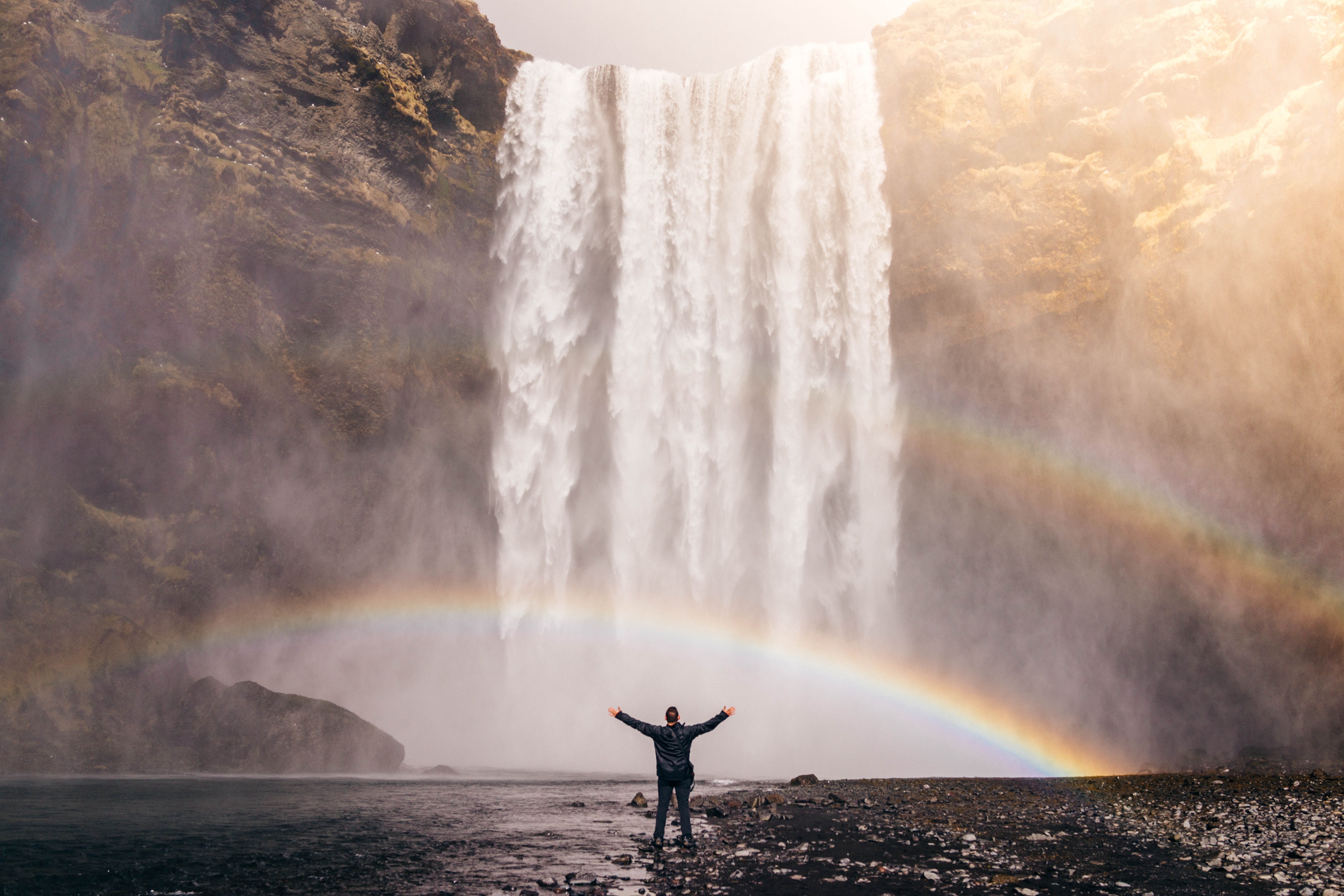 Homem realizado, em uma cachoeira com arco-íris