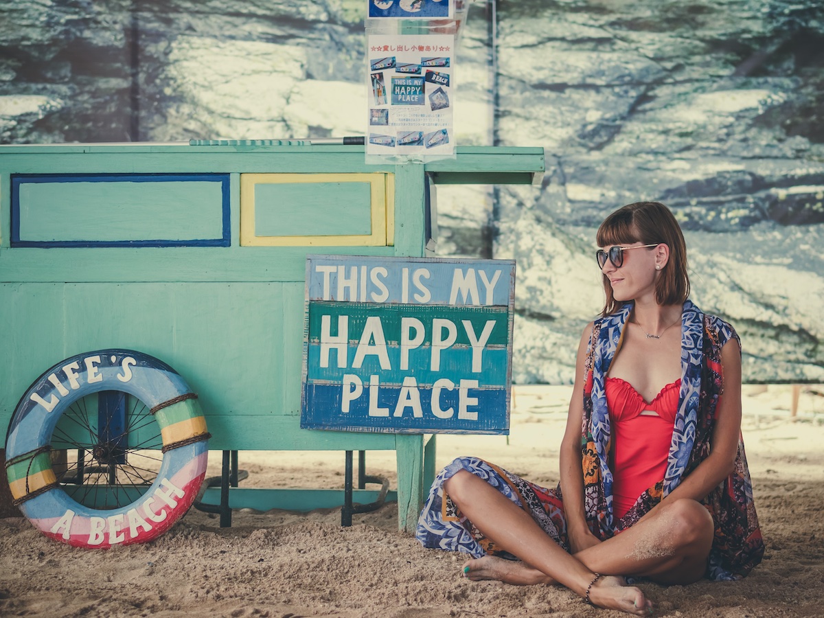 Mulher na praia, com placa de "lugar feliz"